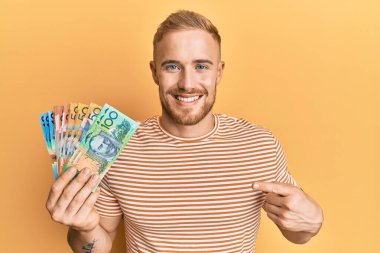 Avustralyalı genç beyaz adam elinde dolarlarla mutlu mesut gülümsüyor. 