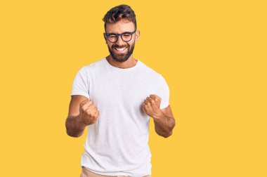 Gündelik kıyafet ve gözlük takan genç İspanyol adam kolları havada ve gözleri kapalı bir şekilde başarıyı kutluyor ve şaşırıyor. Kazanan konsept. 