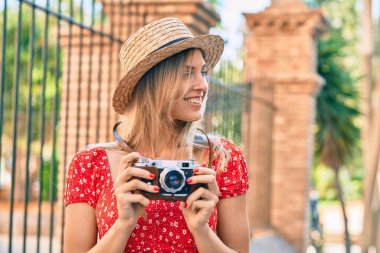 Sarışın, yaz tarzı giyinen genç bir kadın şehirde klasik kamera kullanıyor..