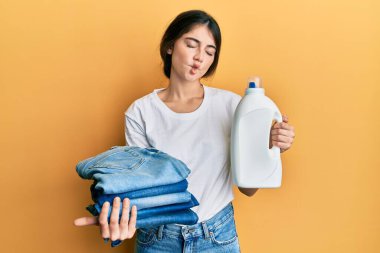 Çamaşır yıkayan, çamaşır deterjanı şişesi ve katlanmış kot pantolon giyen, ağzı açık, şaşı, çılgın ve komik bakışlı genç beyaz kadın.. 