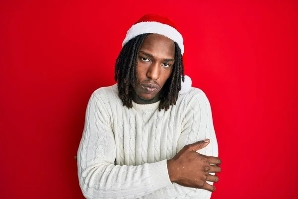 African american man with braids wearing christmas hat shaking and freezing for winter cold with sad and shock expression on face