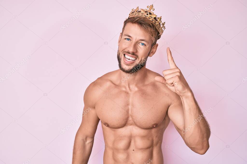 Young caucasian man shirtless wearing king crown pointing finger up with successful idea. exited and happy. number one. 