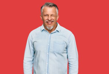 Orta yaşlı, gri saçlı, sıradan kıyafetler giyen, kameraya seksi bir ifadeyle bakan, neşeli ve mutlu yüzlü bir adam.. 