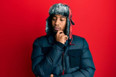 Sakallı, kışlık şapkası ve eli çenesinde paltosu olan, soru soran, düşünceli bir Amerikalı genç adam. Düşünceli bir yüzle gülümsüyor. şüphe kavramı. 