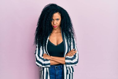Orta yaşlı Afro-Amerikalı kadın gündelik kıyafetler giyiyor şüpheci ve gergin, yüzünde çapraz kollarla onaylamayan bir ifade. negatif kişi. 