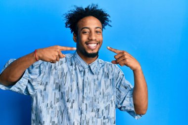 Sakallı, neşeli gülümseyen ve parmaklarıyla ve ağzıyla işaret eden Afro-Amerikan genç adam. diş sağlığı kavramı. 