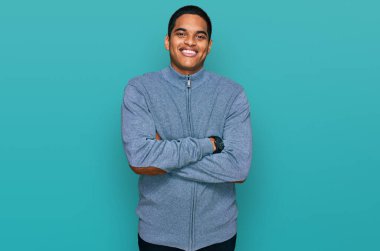 Sıradan bir kazak giyen, kollarını kavuşturup kameraya gülümseyen genç, yakışıklı İspanyol adam. pozitif kişi. 