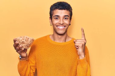 Elinde fıstıkla gülümseyen genç Afrikalı Amerikalı bir adam bir fikir veya soruyla mutlu bir yüzü işaret ediyor. 