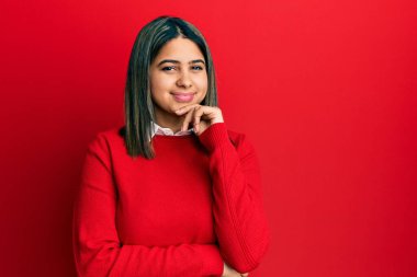 Gündelik kıyafetler giyen genç Latin kadın kameraya kendinden emin bakıyor kollarını kavuşturup gülümseyerek ve çenesini kaldırarak. Olumlu düşünmek. 