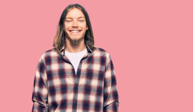 Uzun saçlı, hippi gömleği giyen, yüzünde mutlu ve havalı bir gülümseme olan yakışıklı beyaz bir adam. şanslı kişi. 