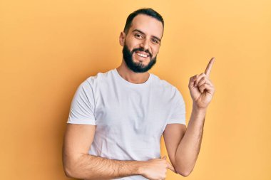 Sakallı, sıradan beyaz tişörtlü genç adam gülümsüyor. 