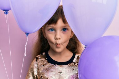 Kafkasyalı küçük kız elinde balonlarla komik suratıyla yanaklarını şişiriyor. Ağzı havayla şişer, havayı yakalar.. 
