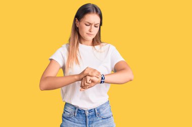Güzel, beyaz tişörtlü beyaz bir kadın. Kol saatini kontrol ediyor. Rahat ve kendinden emin. 