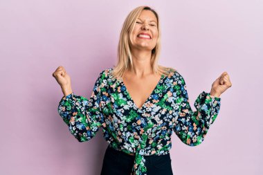 Orta yaşlı, günlük kıyafetler giyen, mutlu ve heyecanlı bir orta yaşlı kadın kollarını kaldırmış, gülümseyen ve başarı çığlıkları atan, kazanan bir jest yapıyor. kutlama konsepti. 