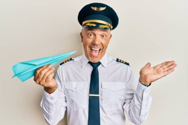 Yakışıklı, orta yaşlı, uçak pilotu üniforması giyen, elinde kağıt uçakla başarıyı kutlayan mutlu bir gülümseme ve elini kaldırmış bir ifadeyle olgun bir adam. 