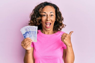 Orta yaşlı, İspanyol bir kadın elinde İsveç banknotları tutarken başparmağıyla ağzını açıp gülümsüyor. 