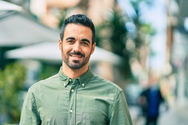 Genç İspanyol adam gülümseyerek şehirde mutlu mesut dikiliyor..