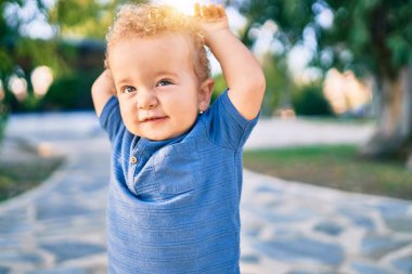 Sevimli ve mutlu küçük çocuk güneşli bir günde parkta eğleniyor. Güzel sarı saçlı erkek çocuk dışarıda oynuyor.