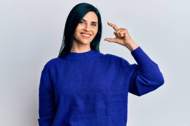 Gündelik kıyafetler giyen, gülümseyen, kendine güvenen, el hareketi yapan, parmaklarıyla işaret yapan, kameraya bakan beyaz bir kadın. ölçüm kavramı. 