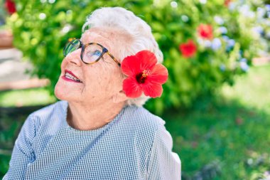 Yaşlı yaşlı, gri saçlı, dışarıda mutlu gülümseyen, dekoratif bir çiçek takan yaşlı kadın.