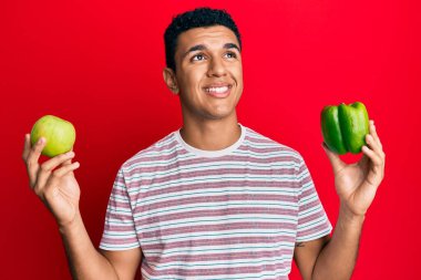 Yeşil elma ve biber tutan genç Arap adam gülümsüyor.. 