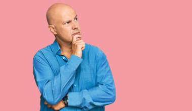 Orta yaşlı kel bir adam, elleri çenesinde gündelik giysiler giyip soru soruyor, düşünceli bir yüz ifadesi var. Düşünceli bir yüzle gülümsüyor. şüphe kavramı. 