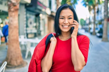 Genç Latin kadın gülümsüyor. Şehirdeki akıllı telefondan konuşuyor..