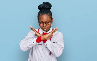 Genç Afrikalı Amerikalı kadın doktor üniforması giyiyor ve steteskop reddediliyor. Kollarını kavuşturup negatif işaret veriyor, kızgın surat yapıyor. 