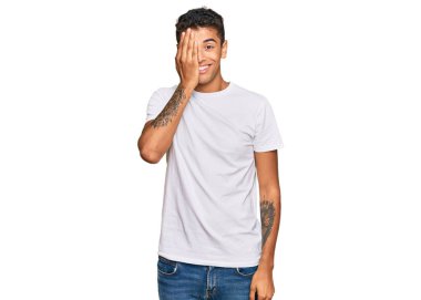 Genç, yakışıklı, Afro-Amerikalı bir adam, günlük beyaz tişört giyiyor, bir gözünü eliyle kapatıyor, yüzünde kendine güvenen bir gülümseme ve sürpriz bir duygu var.. 