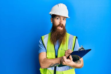 Uzun sakallı, güvenlik kaskı takan, elinde dosyasından bihaber ve kafası karışık bir ifade olan kızıl saçlı bir adam. şüphe kavramı. 