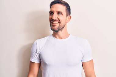 Genç ve yakışıklı bir adam günlük tişört giyiyor. İzole edilmiş beyaz arka plan üzerinde duruyor. Yan tarafa bakıyor, rahat profil pozu veriyor..