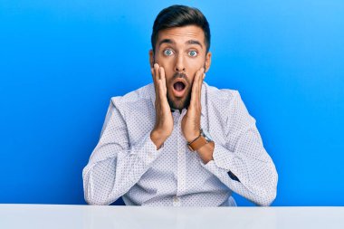 İş elbiseleri giyen yakışıklı İspanyol adam masada korkmuş ve şok olmuş bir şekilde oturuyor, şaşırmış ve şaşırmış bir halde. 