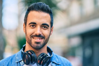 Şehirde kulaklık takarak mutlu gülümseyen genç İspanyol adam..