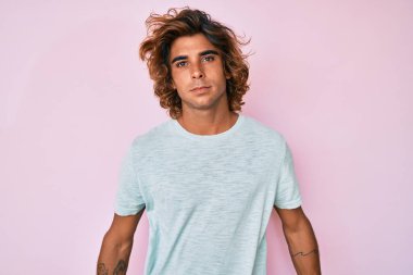 Günlük kıyafetler giyen genç İspanyol adam yüzünde ciddi bir ifadeyle rahatlamış. Basit ve doğal bir şekilde kameraya bakıyorsun.. 