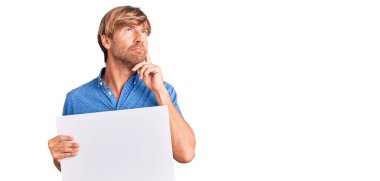 Sakallı, beyaz, yakışıklı bir adam. Satış posteri taşıyor. Ciddi bir yüz ifadesi var. 