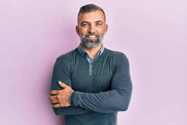 Orta yaşlı yakışıklı, sıradan kıyafetler giyen mutlu yüzlü, kollarını kavuşturup kameraya bakan bir adam. pozitif kişi. 