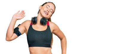 Güzel sarışın kadın spor kıyafetleri giyiyor ve kulaklık takıyor. Yorgun, rahat, uykulu ve sabahın erken saatlerinde esniyor. 