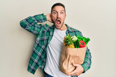 Yakışıklı ve sakallı bir adam. Elinde poşet dolusu alışveriş torbası var. Delicesine korkmuş ve elleri başında korkmuş. 