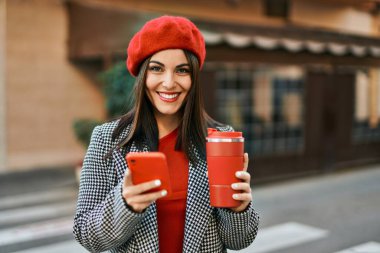 Genç İspanyol kadın akıllı telefon kullanıyor ve şehirde kahve içiyor..