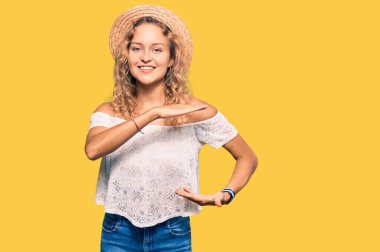 Yazlık şapkalı güzel beyaz kadın. Elleriyle işaret ediyor. Büyük ve büyük beden işareti, ölçü işareti. Kameraya bakıp gülümsüyor. ölçüm kavramı. 