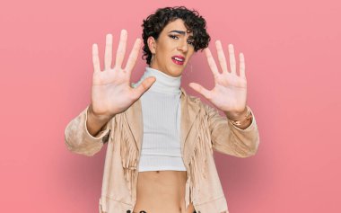 Makyaj yapan yakışıklı bir adam ve kadın kıyafetleri. Avuç içi hareketlerini, sinirli ve hayal kırıklığına uğramış ifadelerini durduruyorlar. 