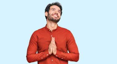 Gündelik giysiler giyen genç İspanyol adam elleri bağlı yalvarıyor ve dua ediyor. Yüzünde umut ifadesi var. Çok duygusal ve endişeli. Yalvarıyor. 