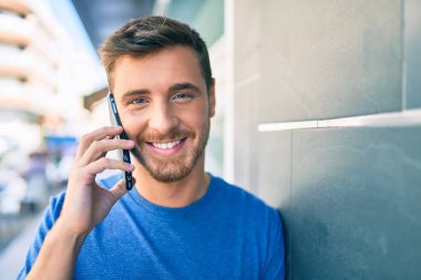 Genç beyaz adam gülümsüyor. Şehirdeki akıllı telefondan konuşuyor..