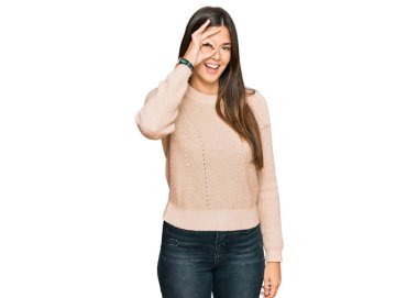 Genç esmer kadın sıradan bir kazak giyiyor. El hareketleriyle gülümsüyor ve mutlu yüzüyle parmaklarının arasından bakıyor.. 