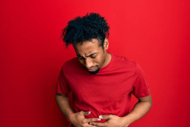 Sakallı, kırmızı tişörtlü, midesi üstünde genç Afro-Afrikalı bir adam. Çünkü hazımsızlık, acı verici bir hastalık ve kendini kötü hissediyor. Ağrı kavramı. 