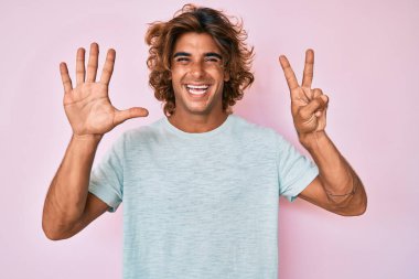 Gündelik kıyafetler giyen genç İspanyol adam yedi numarayı gösterip işaret ederken kendinden emin ve mutlu bir şekilde gülümsüyor.. 