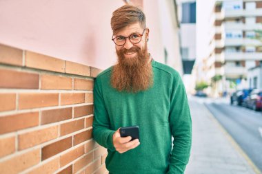 Kızıl saçlı, mutlu gülümseyen ve şehirde akıllı telefon kullanan genç bir İrlandalı..