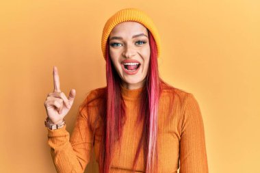Kafkasyalı, yün şapkalı genç bir kadın başarılı bir fikri işaret ediyor. Heyecanlı ve mutlu. Bir numara.. 