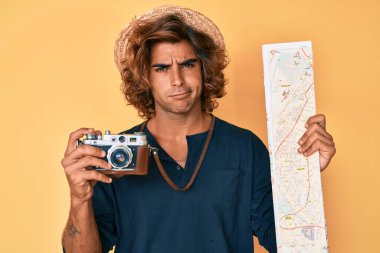 Klasik fotoğraf makinesi ve şehir haritası tutan genç İspanyol bir adam. Hiçbir şeyden habersiz ve kafası karışmış bir ifade. şüphe kavramı. 