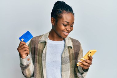 Genç Afro-Amerikalı kadın elinde akıllı telefon ve kredi kartı ile mutlu ve havalı bir gülümsemeyle gülümsüyor. diş gösterme. 
